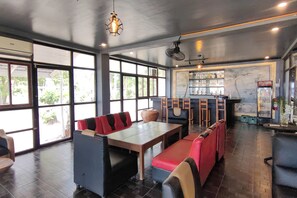 Un restaurante con área de bar, asientos con cojines rojos y negros, y un gran ventanal que ofrece vistas al exterior.