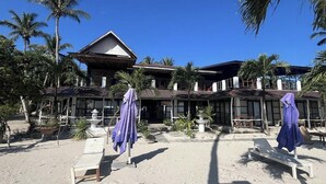 Un hotel frente a la playa con varias habitaciones, un porche cubierto y sillas para la playa.