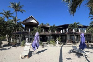 Un hotel frente a la playa con varias habitaciones, un porche cubierto y sillas para la playa.