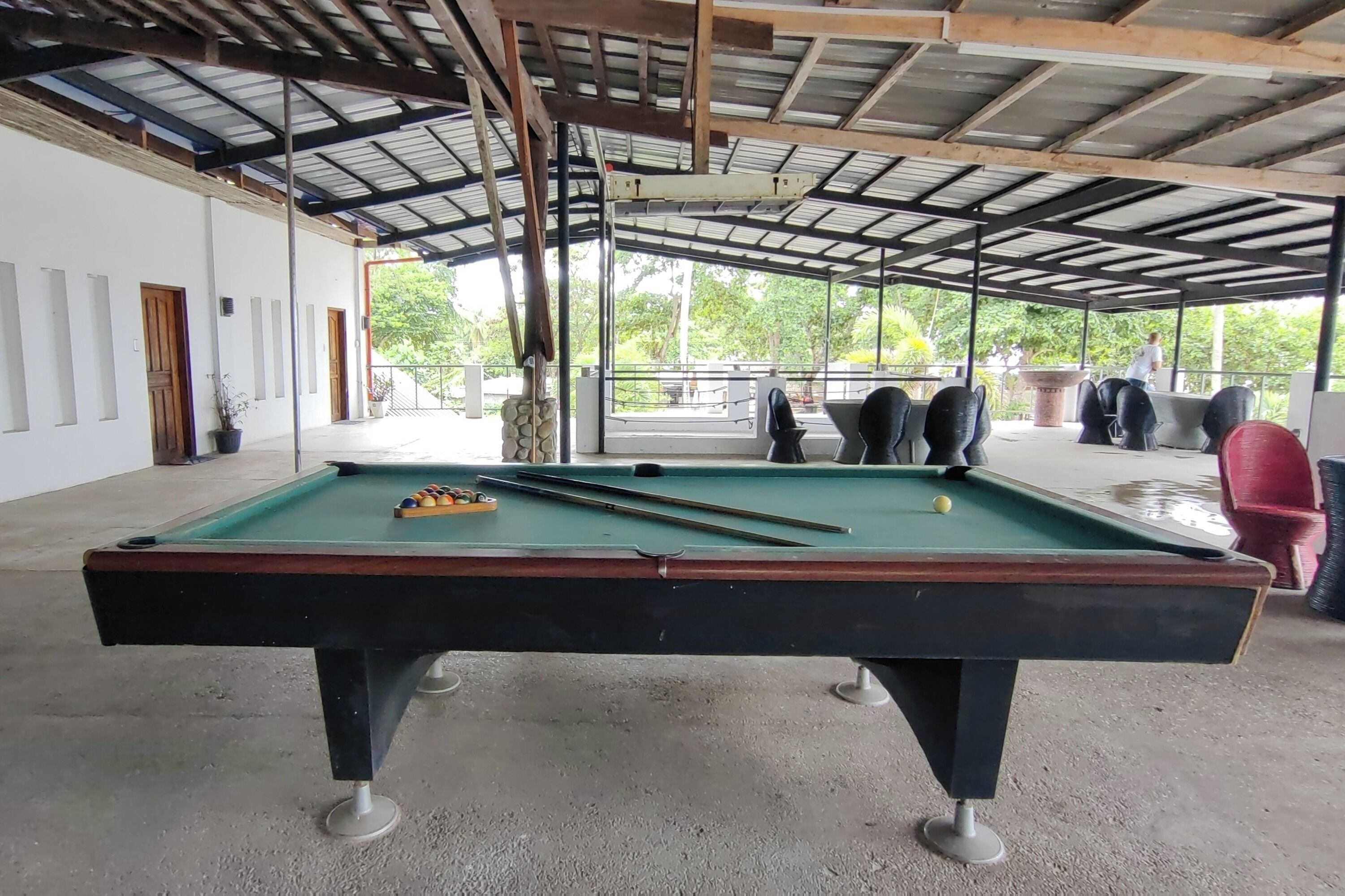 A pool table with balls, a ceiling with metal beams, and a view of greenery outside.