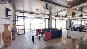 Un vestíbulo espacioso con área de descanso, ventanas amplias y ventiladores de techo.