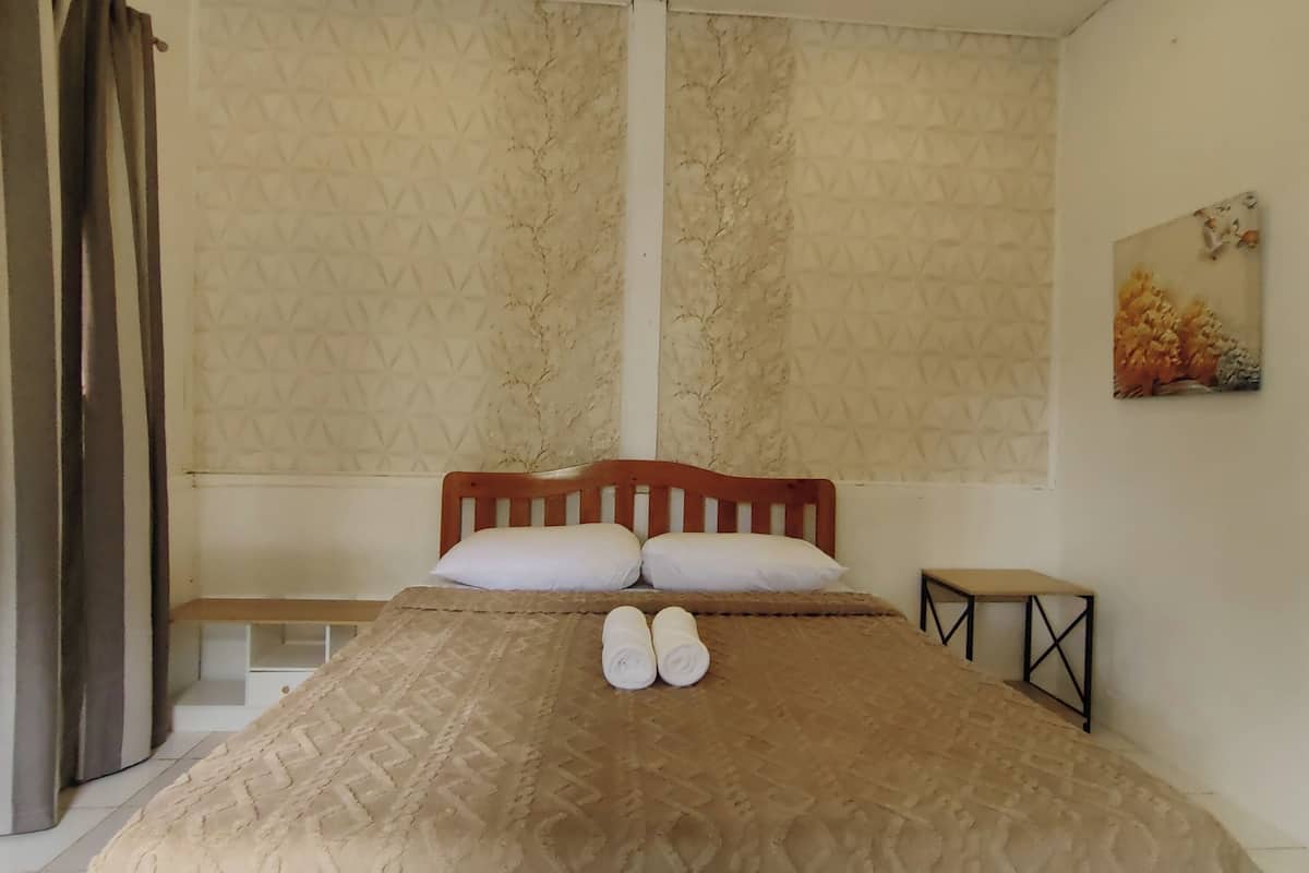 Una cama bien hecha con una colcha estampada, dos almohadas y toallas enrolladas sobre la cama.