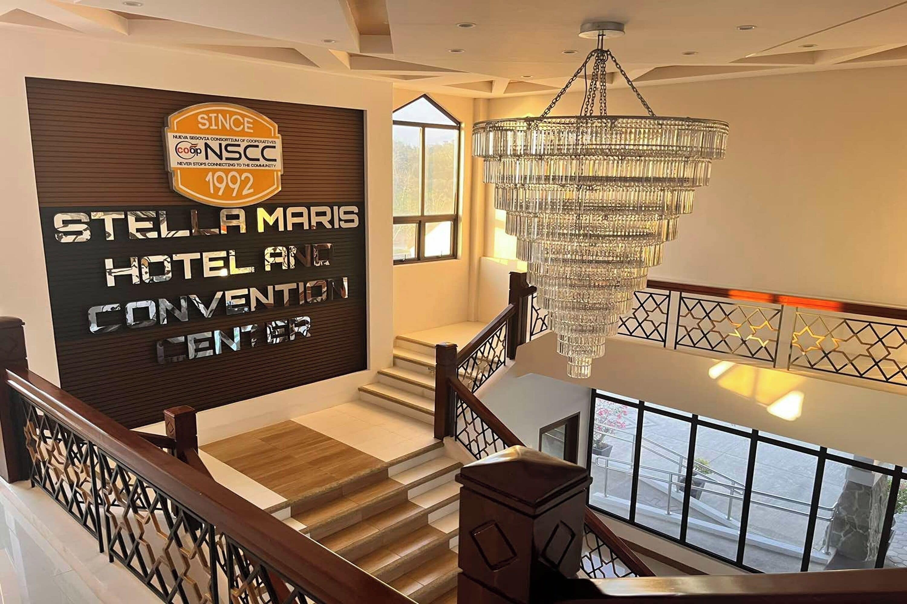 Una scala con un lampadario, una segnaletica per l'Hotel e Centro Congressi Stella Maris, e vista esterna.