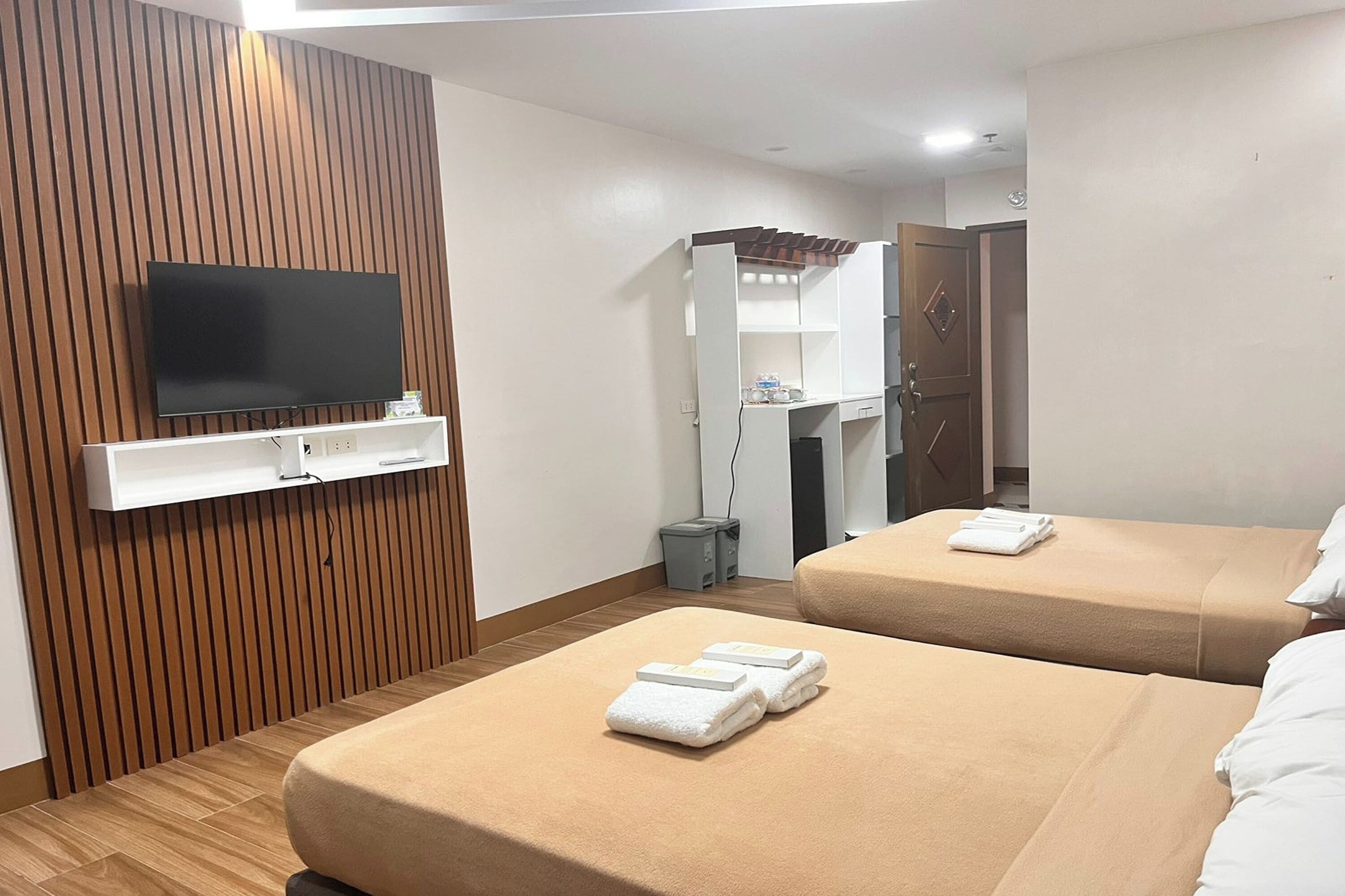 Une chambre d’hôtel avec deux lits, un téléviseur fixé au mur, une armoire et une petite poubelle.