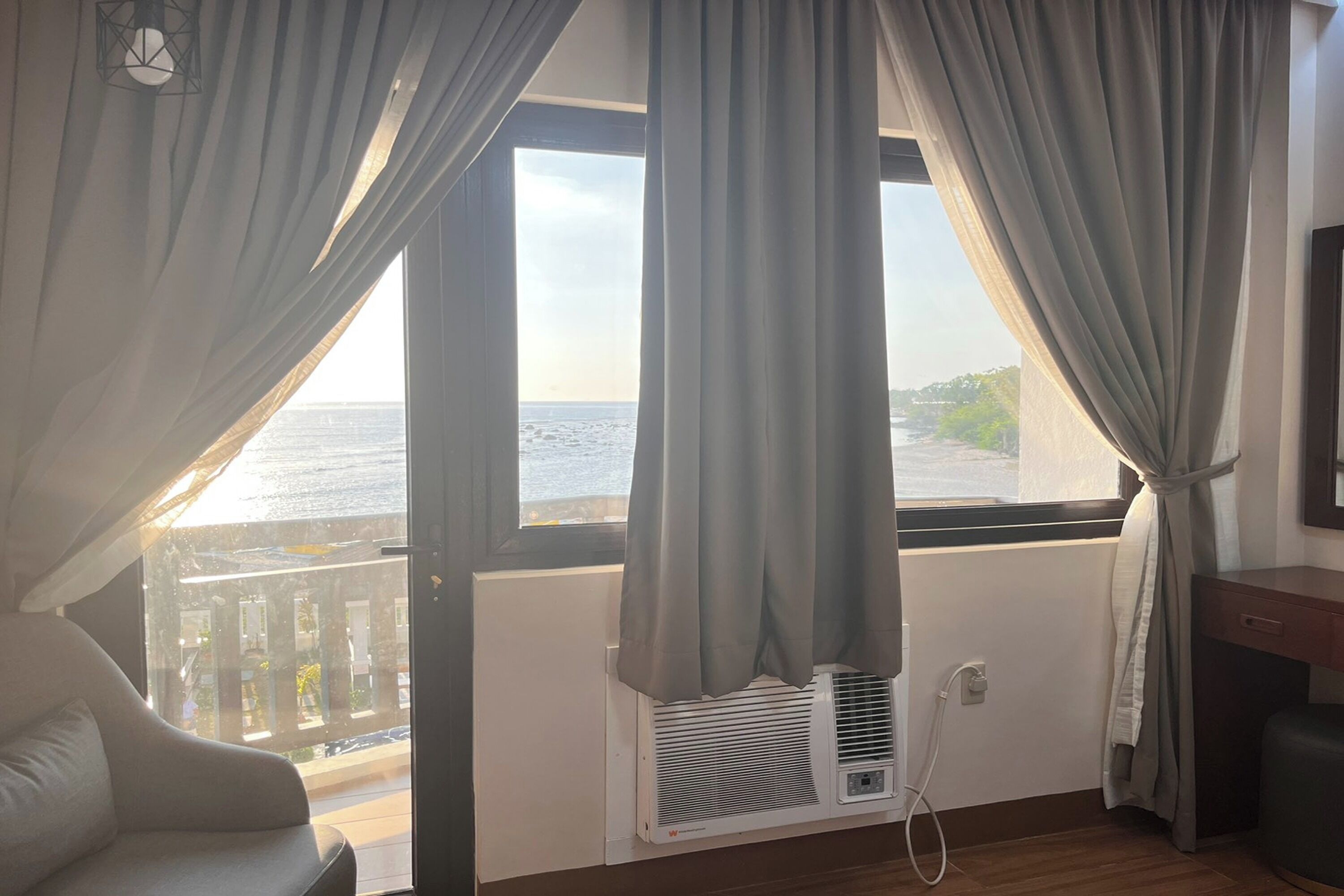 Habitación con vista al mar, unidad de aire acondicionado blanca, una silla y suelo de madera.