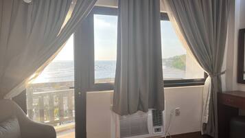 Habitación con vista al mar, unidad de aire acondicionado blanca, una silla y suelo de madera.