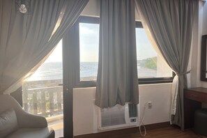 A room with a view of the sea, a white air conditioning unit, a chair, and a wooden floor. - Nscc Stella Maris Hotel & Convention Center (Cabugao)