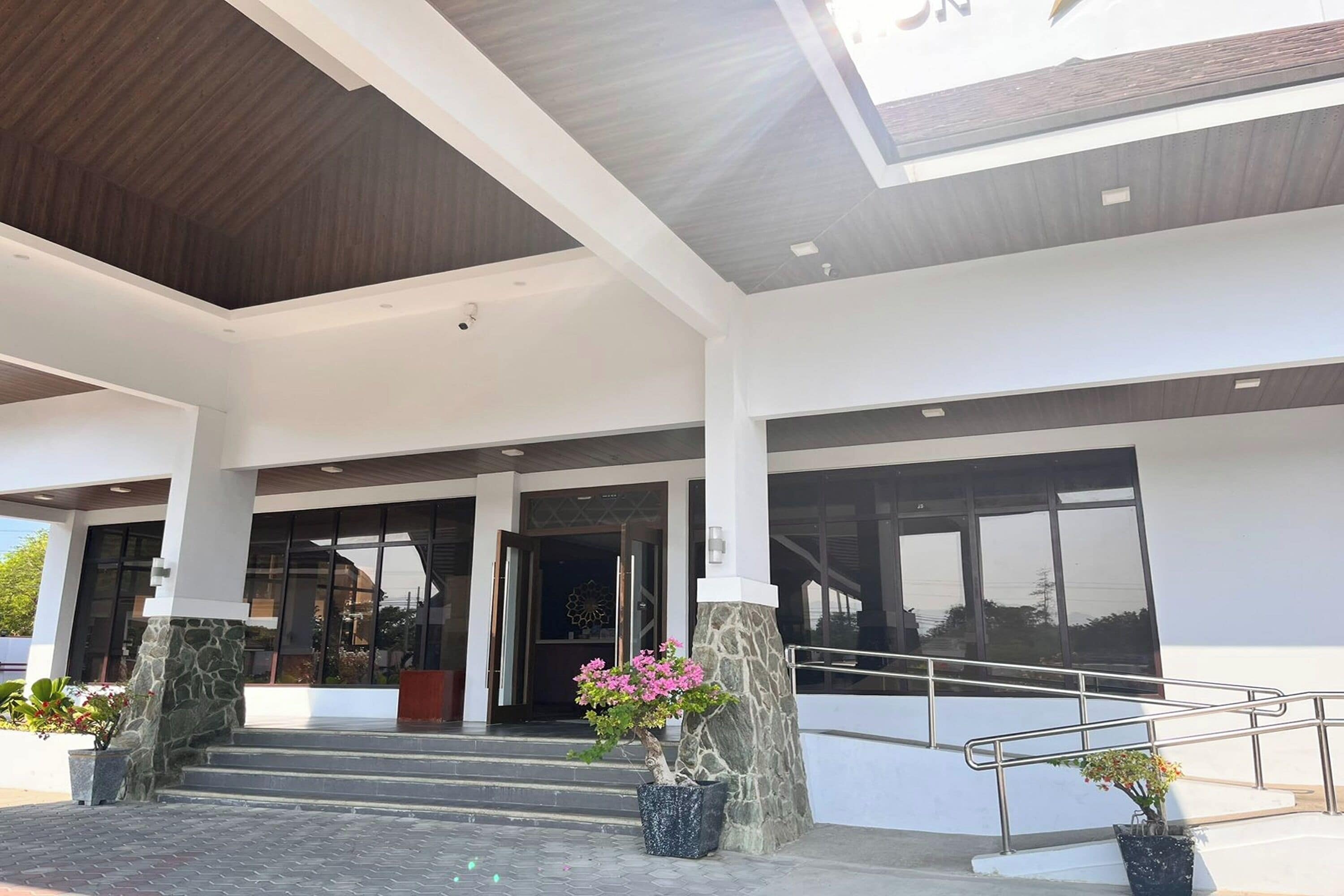 A modern building entrance with a stone column, steps leading up to a door, and potted plants.
