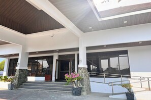 A modern building entrance with a stone column, steps leading up to a door, and potted plants. - Nscc Stella Maris Hotel & Convention Center (Cabugao)