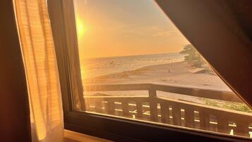 A window view of a beach with a wooden deck and a railing.