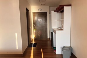 A hallway with a wooden floor, a door with a diamond-shaped window, and a white cabinet with a shelf.