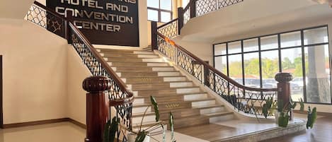 A staircase with a wooden handrail and metal railings, leading to a room with large windows and a sign for Stella Maris Hotel and Convention Center.