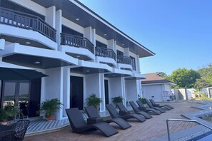 A hotel with multiple balconies, a pool area with sun loungers, and potted plants.