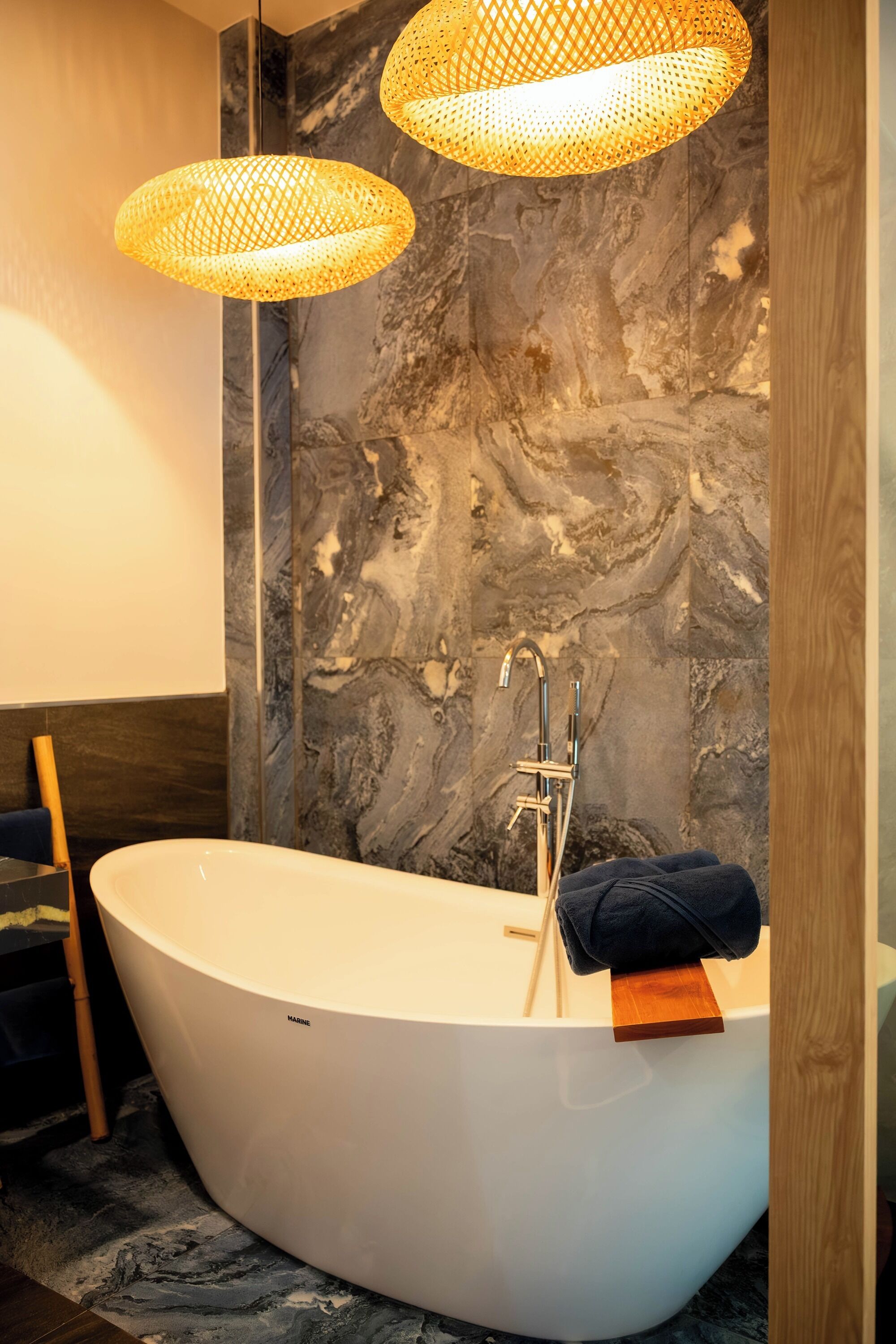 Un bagno moderno con una vasca da bagno indipendente, una sedia in legno e due lampade a sospensione in fibra.