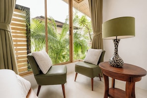 Una habitación con dos sillas verdes, una mesa de madera con una lámpara y un ventanal con persianas.