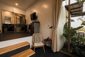 Una habitación moderna con un banco de madera, un sillón acolchado, una mesita con tetera y un televisor en la pared.