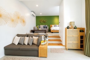 Una sala moderna con un sofá gris, una mesita de madera, una pared de acento verde y una escalera que lleva a otra habitación.