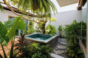 A private garden with a hot tub, surrounded by lush plants and a wooden deck.