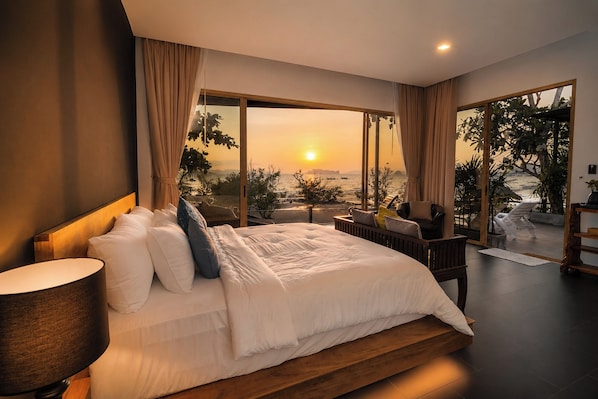 Un dormitorio con una cama grande, una mesita de noche, una lámpara y vistas al atardecer sobre el agua.