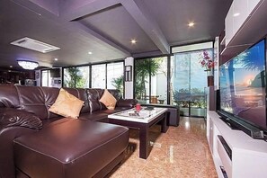 A modern living room with a leather sofa, a coffee table, and a large flat-screen TV. - Exotica Pool Villa Encore (Chonburi)