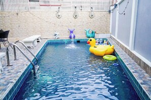 A swimming pool with a diving board, lounge chairs, and decorative items. - Exotica Pool Villa Encore (Chonburi)