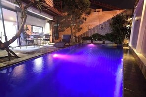 Ein Pool mit blauer Färbung, umgeben von einer Terrasse mit Stühlen und einem Tisch.