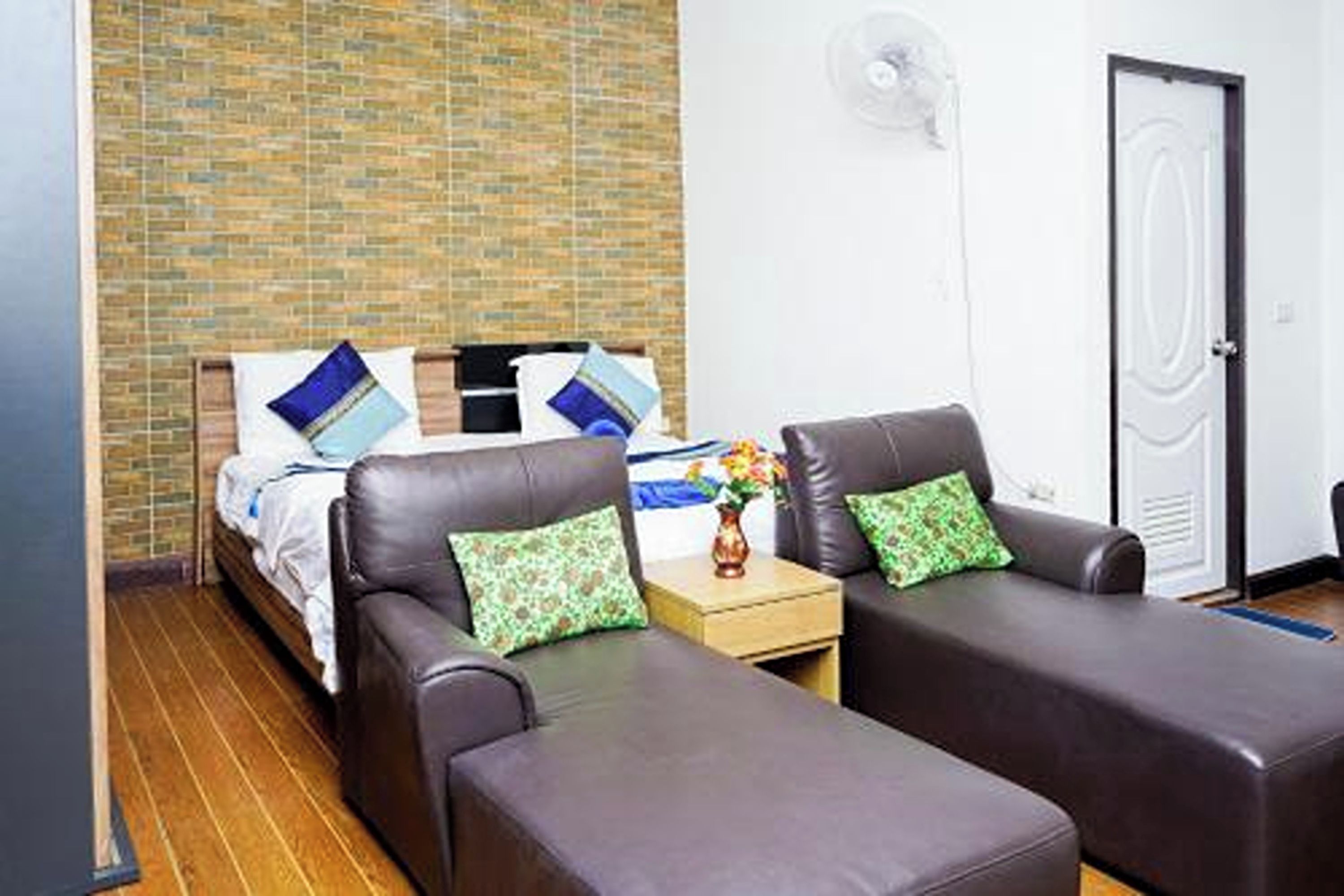 Une chambre d’hôtel avec un lit, deux fauteuils, une petite table avec un vase et une porte.