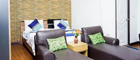 A hotel room with a bed, two armchairs, a small table with a vase, and a door.