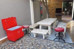 An outdoor patio area with a red cooler, white tables, and matching stools. - Exotica Pool Villa Encore (Chonburi)