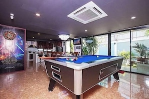 A pool table in a room with a large window, a dartboard, and a chandelier. - Exotica Pool Villa Encore (Chonburi)