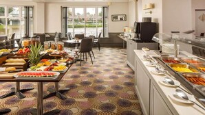 Comedor de hotel con servicio de comidas tipo buffet, un televisor y vistas al exterior.