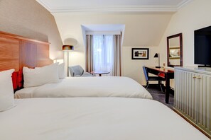 Habitación de hotel con dos camas, un escritorio, una silla, un televisor y una ventana con cortinas.