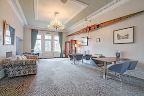 Une chambre d’hôtel avec un tapis à motifs, un canapé, une table à manger avec des chaises, un lustre et des tableaux encadrés accrochés aux murs.