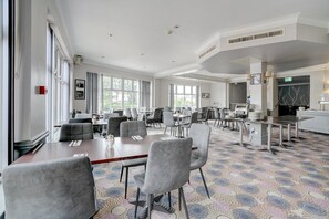A spacious conference room with multiple tables and chairs, large windows, and a patterned carpet.