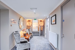 A hotel hallway with a reception desk, chairs, a lamp, a framed picture, and a sign reading 'The Conservatory.'