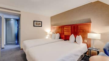 A hotel room with two beds, a wooden headboard, a framed picture on the wall, and a desk with a lamp.