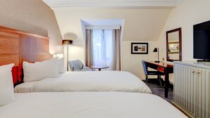 Habitación de hotel con dos camas, un escritorio, una silla, un televisor y una ventana con cortinas.