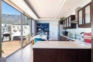 A modern kitchen with a large island, a dining area with a view, and a dining table set for four. - Luxurious 2-Bedroom Penthouse with Stunning Views in Central Cape Town (Cape Town)
