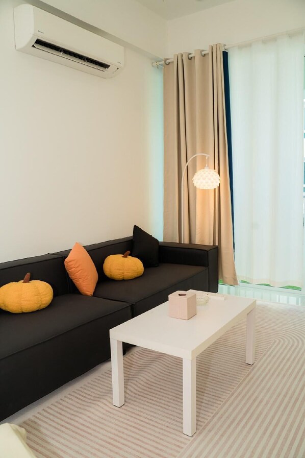 Una sala de estar moderna con un sofá negro, cojines naranja y amarillos, una mesa de centro blanca y una lámpara colgante.