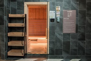 Saunassa on puulankutuksesta tehty seinäpaneeli, puinen hyllykkö sekä kyltti, jossa kerrotaan saunan aukioloajat ja käyttösäännöt.