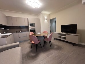 Eine moderne Küche mit eingebauten Geräten, ein Essbereich mit rosa Stühlen und ein Fernseher auf einem Standfuß.