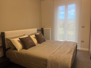 Un dormitorio con una cama, dos almohadas, un radiador y una ventana con vistas.