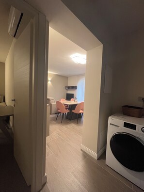 Un lavadero con lavadora y secadora de carga frontal, una zona de comedor con mesa y sillas, y un pasillo que conduce a una sala de estar.