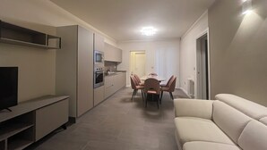 Ett modernt kök med inbyggda vitvaror, en matplats med bord och stolar samt ett vardagsrum med en soffa.