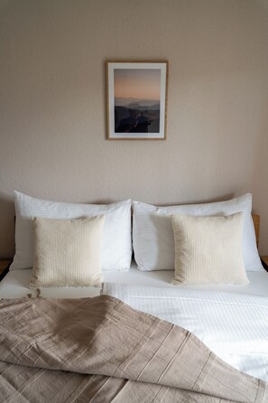 A neatly made bed with white linens and a beige throw blanket, a framed picture on the wall, and a textured beige wall. - 4Seasons | Morschach | Family Apartment | Mountain View (Morschach)