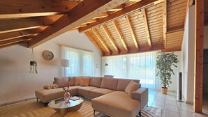 Un salon spacieux avec un grand canapé d’angle, une table basse en verre et un plafond en bois.