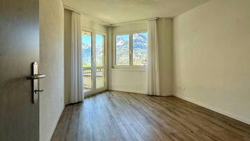 Une pièce spacieuse avec un plancher en bois, un ventilateur de plafond et une vue sur les montagnes grâce à de grandes fenêtres.