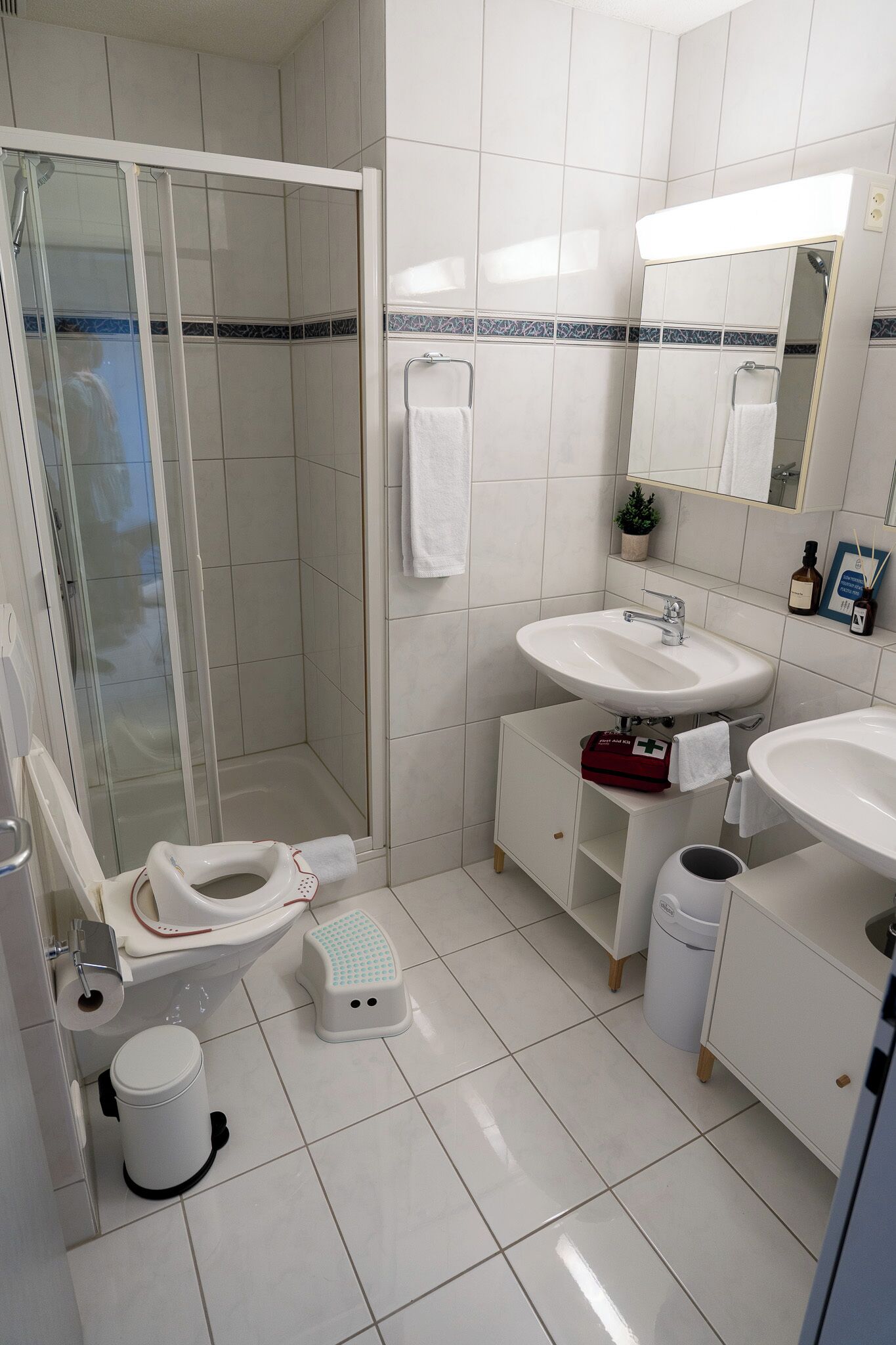 Een moderne badkamer met een glazen douchecabine, toilet, een bidet, een wastafel en een prullenbak.