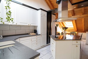 A modern kitchen with white cabinetry, a central island, and a wooden ceiling. - 4Seasons | Morschach | Family Apartment | Mountain View (Morschach)