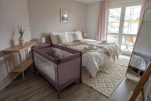 Ein Schlafzimmer mit einem Bett, einem Babybett, einem Nachttisch, einer Lampe, einem Teppich und einem Fenster mit Blick.